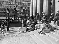 Hötorget 8. Folk sitter på trappan till Konserthuset i vårsolen.