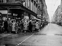 Hörnet Drottninggatan och Klarabergsgatan. Gustaf VI Adolf fyller 70 år och åker i kortege genom staden. Längs kortegens väg stod stockholmare och väntade. T.h. vy Drottninggatan norrut.