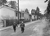 Västberga, Korpmossen. Två barn promenerar i småstugeområde. I bakgrunden LM Erikssons torn.