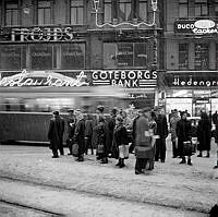 Stureplan 2-4. Folk väntar på buss/spårvagn i snöyran. I bakgrunden syns Hedengrens Bokhandel, Göteborgs Bank och Fröjds Herrkläder.