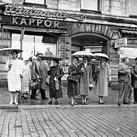 Vasagatan 22. Folk på väg över gatan i ett regnigt och blött Stockholm.