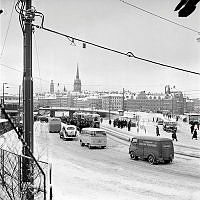 Katarinavägen. Bilar tar sig fram genom snön vid Slussen. Vy mot Gamla Stan.