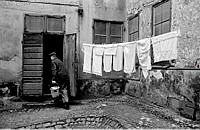 Norra Smedjegatan. Kullerstensbelagd gård med hängande tvätt och en man med en hink.