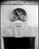 Stenskulptur, kartusch, ovan porten till Vindragarlagets härbärge, Stora Hoparegränd 6. Kartuschen avbildar vindragarens arbetsredskap, stockkniv och sugare.