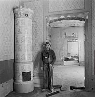 Rumsinteriör under ombyggnad med kakelugn och byggnadsarbetare.