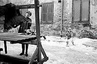 Norra Smedjegatan. Kvinna som piskar mattor på en bakgård  och ett barn som skottar snö.