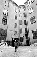 Norra Smedjegatan 5. Gårdsmiljö med ett barn på gården som pratar med sin mamma som ser ut genom fönstret på fjärde våningen.