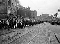 Begravningståg och katafalker på Skeppsbron med kvarlevorna efter Salomon August Andrée, Nils Strindberg och Knut Fraenkel från Andréexpeditionen. I fonden Kungliga Operan.